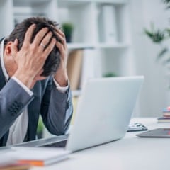 Homem com as mãos na cabeça indicando preocupação, sentado em frente ao computador